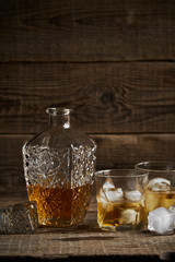 Whiskey with ice in glasses, rustic wood background, copy space 