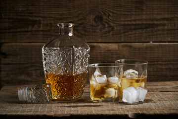 Whiskey with ice in glasses, rustic wood background, copy space 