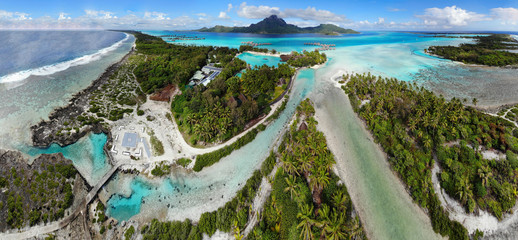 Aerial panoramic landscape view of the island of Bora Bora in French Polynesia with the Mont Otemanu mountain surrounded by a turquoise lagoon, motu atolls, reef barrier, and the South Pacific Ocean - obrazy, fototapety, plakaty
