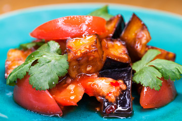 Salad of tomatoes and fried eggplant with sauce on blue plate