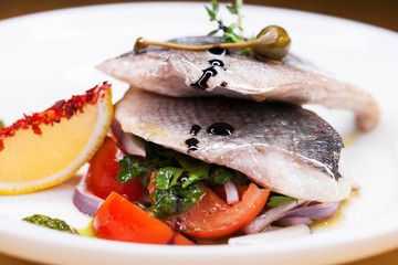 Grilled Dorado fish with onion and lemon slice on white plate