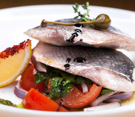 Grilled Dorado fish with onion and lemon slice on white plate