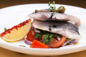 Grilled Dorado fish with onion and lemon slice on white plate