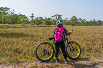 Asian female cyclist standing on grass field with mountain bike