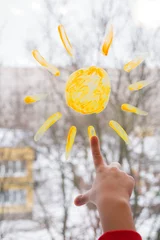 Children's hand stretches to the sun painted on the window © Mariia