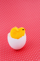 Yellow toy chicken  hatched egg shell on a red background. Easter background.