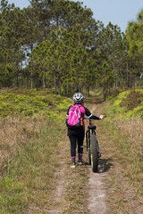 Female cyclist walking on dirt road with mountain bike