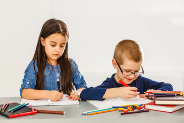 Two smiling little kids at the table draw with crayons, isolated on white