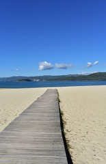 Fototapeta na wymiar Beach with wooden boardwalk, bright sand and blue sky. Galicia, Spain.