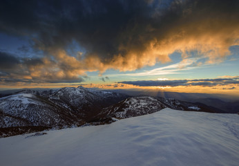 Golden clouds by the sunset light over snowy mountains