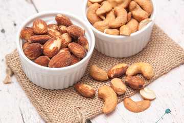 Almonds and cashews in the small cup on the sackcloth and old white woodden background 