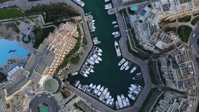 Video shows marine with a lot of sailing boats parked. The marine is surrounded by luxury condominium.
