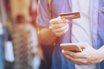 young male hands holding credit card and using mobile smart phone Standing in front of the clothing store. Online shopping purchase Sell or Payment.	