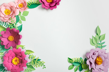 top view of multicolored paper flowers and green plants with leaves on grey background