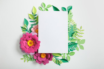top view of white blank card on paper flowers and green leaves on grey background