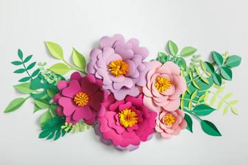top view of pink and lilac paper flowers with green leaves on grey background