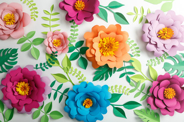 top view of colorful paper flowers and green leaves on grey background