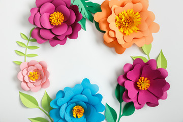 top view of multicolored paper flowers and green leaves on grey background
