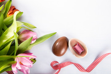 Wielkanocne, wiosenne tlo. Czekoladowe jaja i róźowe tulipany na białym tle.