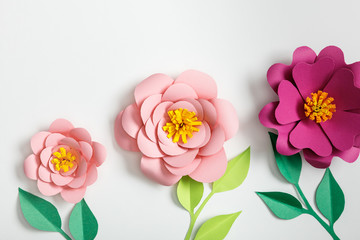 top view of pink paper flowers and green plants with leaves on grey background