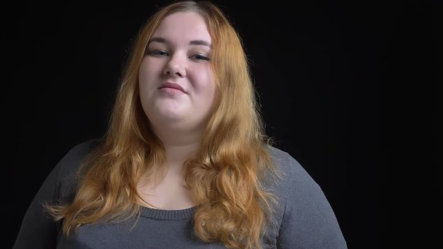 Closeup shoot of young overweight caucasian female looking at camera and smiling seductively with background isolated on black
