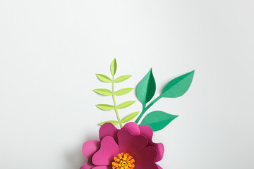 top view of pink paper flower and green plants on grey background