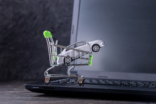 Shopping basket with car on laptop keyboard on dark background. Concept of online shopping vehicles on the Internet