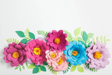 top view of multicolored paper flowers and green leaves on grey background