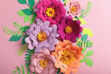 top view of paper flowers, green and yellow leaves on pink background
