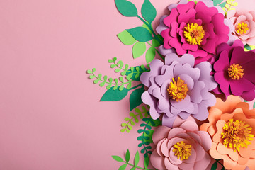top view of colorful paper flowers and green leaves on pink background