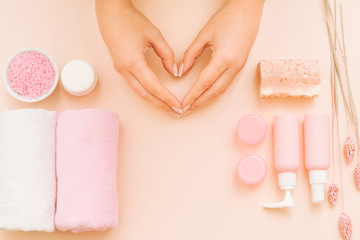 Hands health and beauty care. Woman hands making heart shape symbol. Treatment cosmetic set on coral pink background.