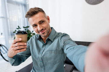 cheerful  man talking selfie while holding paper cup in modern office