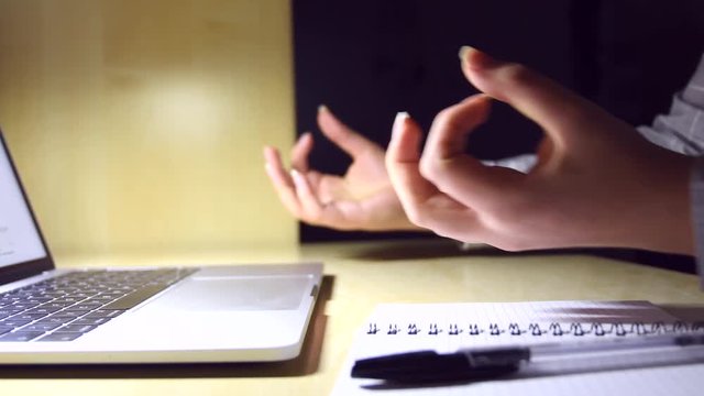 young female hands doing yoga on a minimal office workplace with a laptop, a notebook and a pen, for stress relief during work