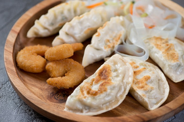 Close-up of different fried potstickers and panko breaded shrimps on a wooden serving tray