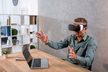 businessman wearing virtual reality headset while sitting in office near laptop