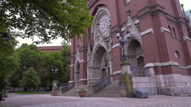Static shot of St Johns Church, green leaves and branches, waving in the wind, on a cloudy, summer day, in Ullanlinna, Helsinki, Finland