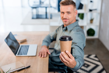 selective focus of paper cup in hand of cheerful businessman in office