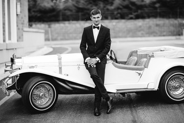 Elegant fiance in a black suit. Man standing near old car