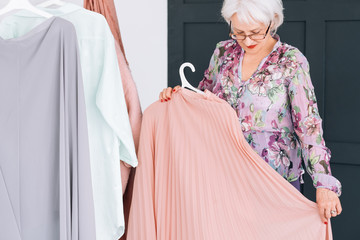 Wealthy senior lifestyle. Fashion clothes shopping. Confident elderly lady trying on elegant garment.