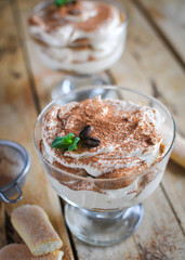 Close-up of classic tiramisu cake in a glass with fresh mint, on wooden background