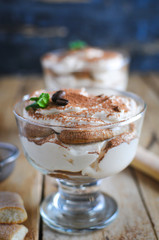 Close-up of classic tiramisu cake in a glass with fresh mint, on wooden background