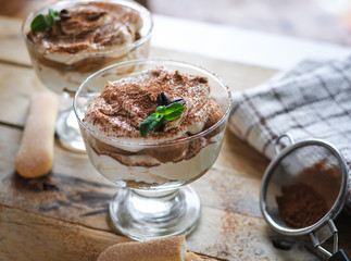 Close-up of classic tiramisu cake in a glass with fresh mint, on wooden background