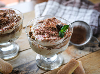 Close-up of classic tiramisu cake in a glass with fresh mint, on wooden background