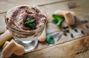 Close-up of classic tiramisu cake in a glass with fresh mint, on wooden background
