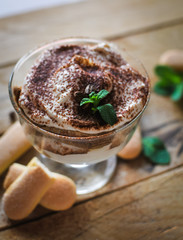 Close-up of classic tiramisu cake in a glass with fresh mint, on wooden background