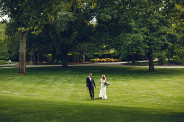 Beautiful bride in a long white dress. Handsome groom in a black suit. Couple in a summer park