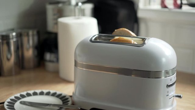 Breakfast bagel bun being put into white toaster by male hand.