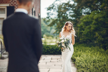 Fototapeta premium Beautiful bride in a long white dress. Handsome groom in a black suit. Couple in a summer park