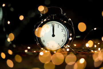 Fototapeta na wymiar alarm clock on the eve of the holiday shrouded in garland