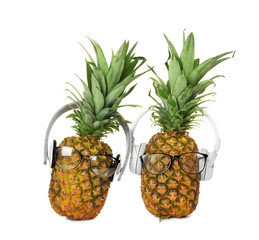 Fresh pineapples with headphones and glasses on white background
